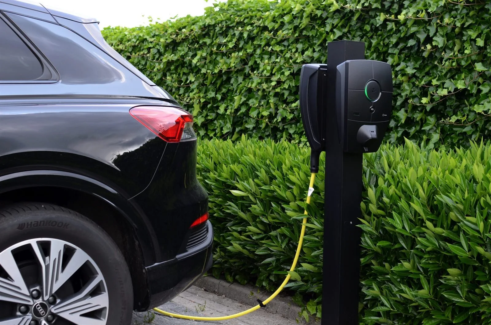 Elektrische auto aangesloten op een laadpaal naast een groene haag